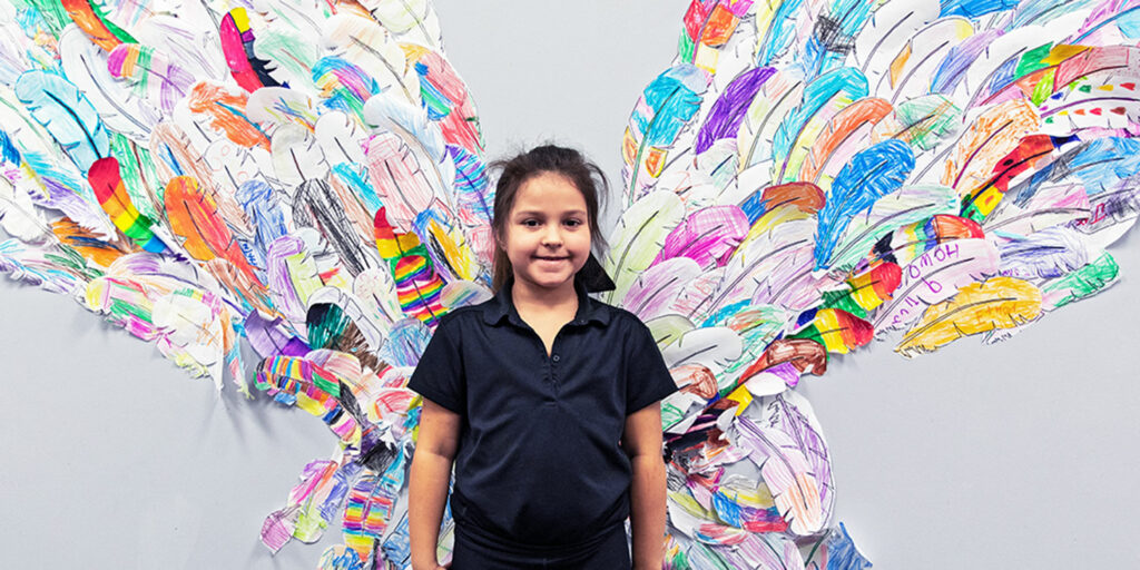 Smiling student standing in front of a feather butterfly wing wall display.